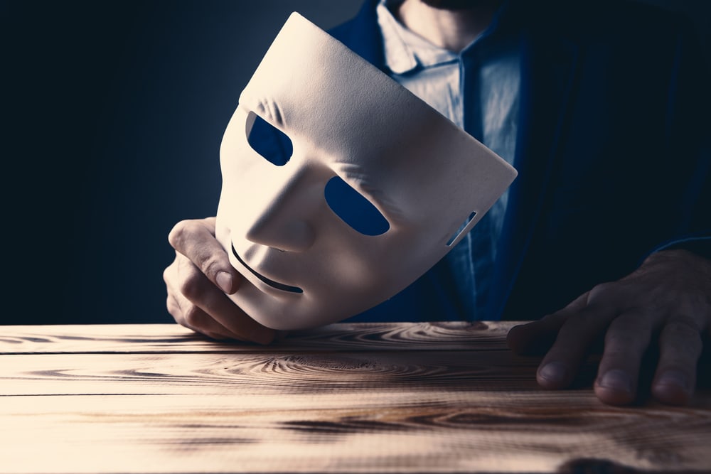 fraud imposter syndrome example of person holding mask in hand